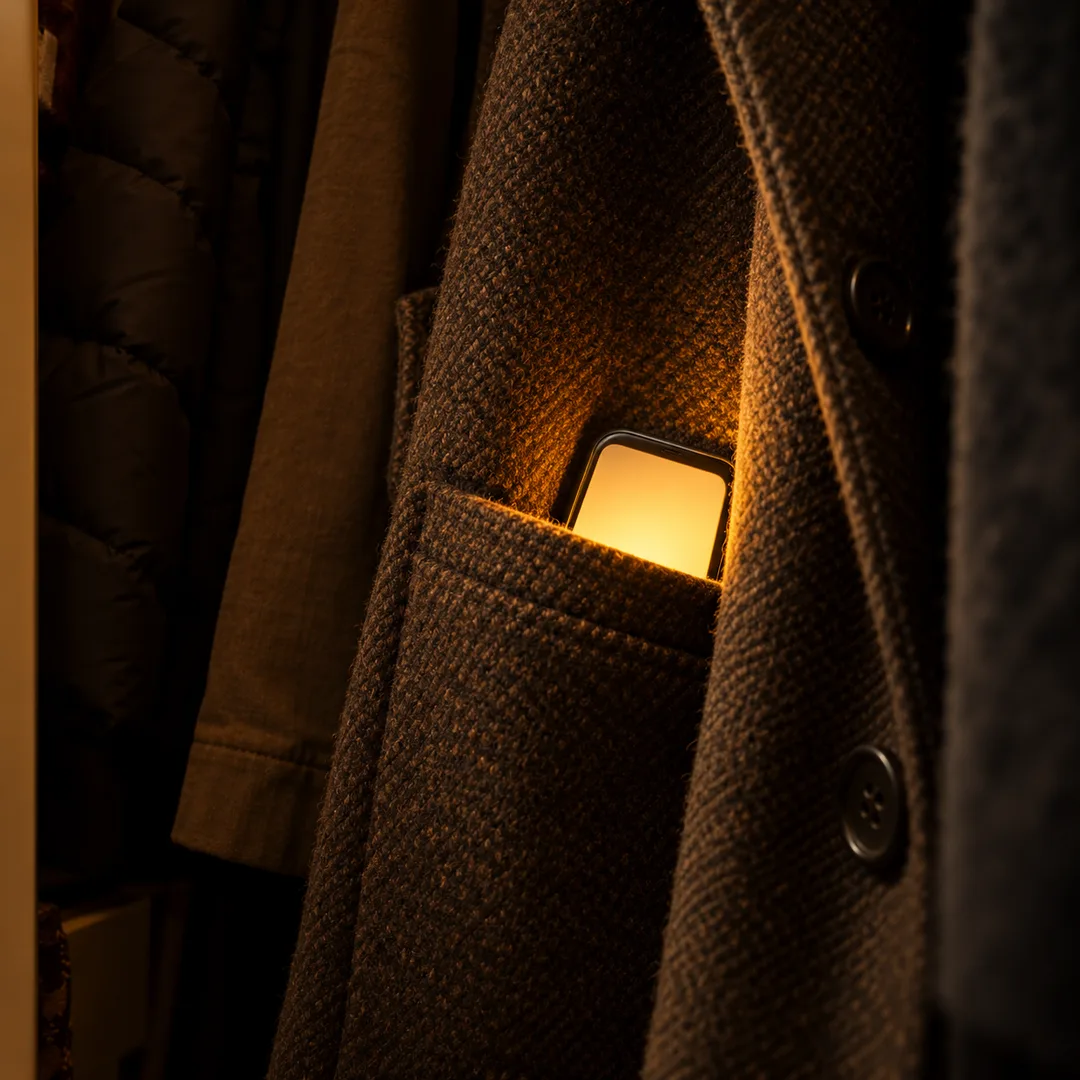 A second phone glows inside the pocket of a stored coat